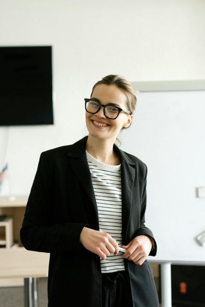 Smiling businesswoman in formal attire wearing eyeglasses in a modern office.