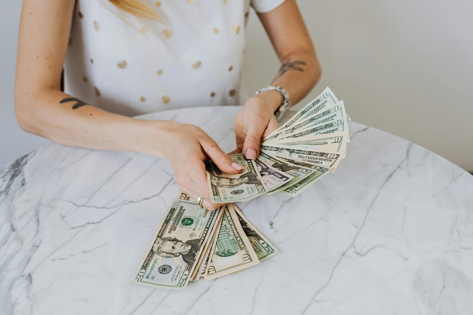 Close-up of a person counting US dollar bills on a luxurious marble table, symbolizing wealth and finance.