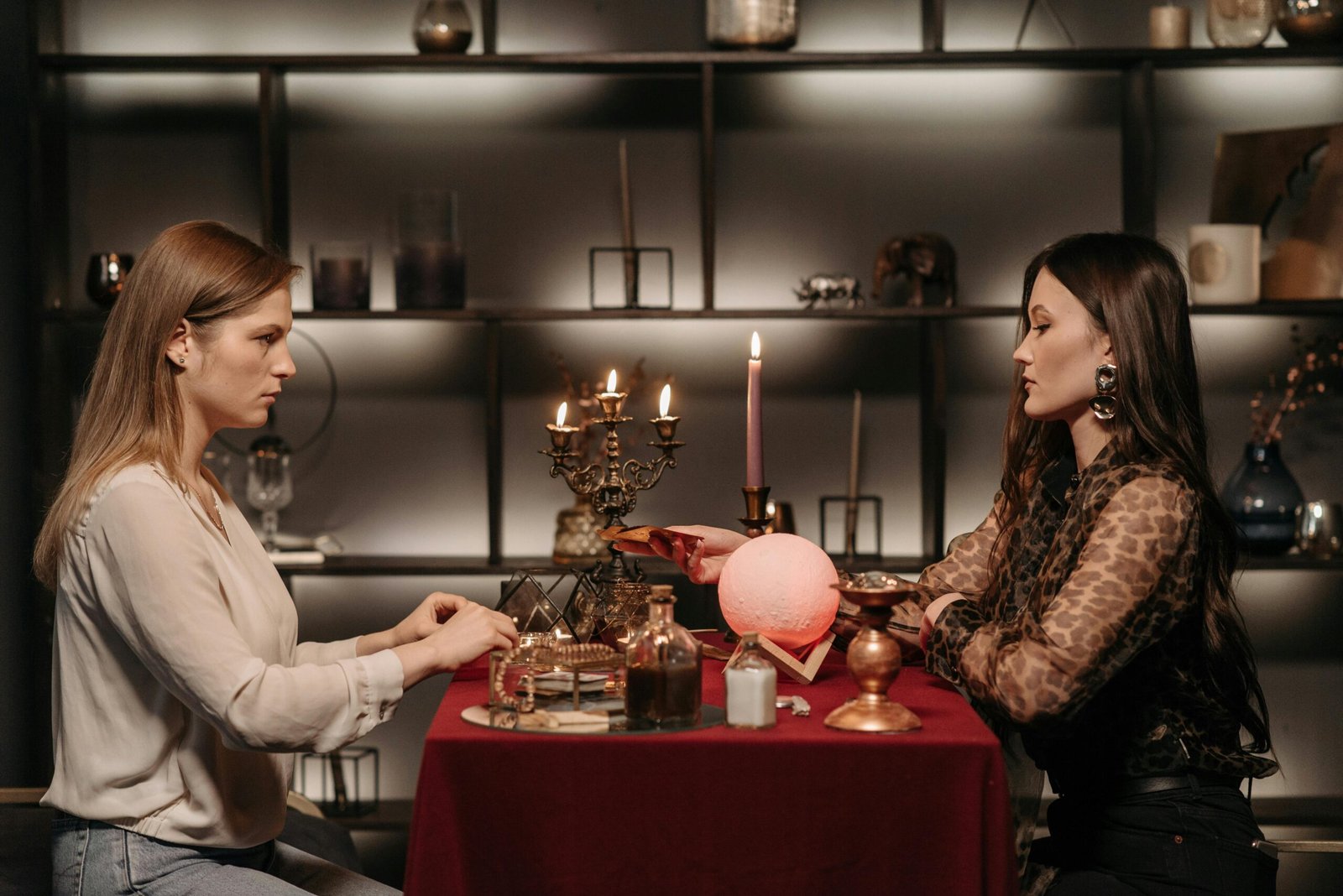 Two women engaged in fortune telling with a crystal ball in a mystical indoor setting.