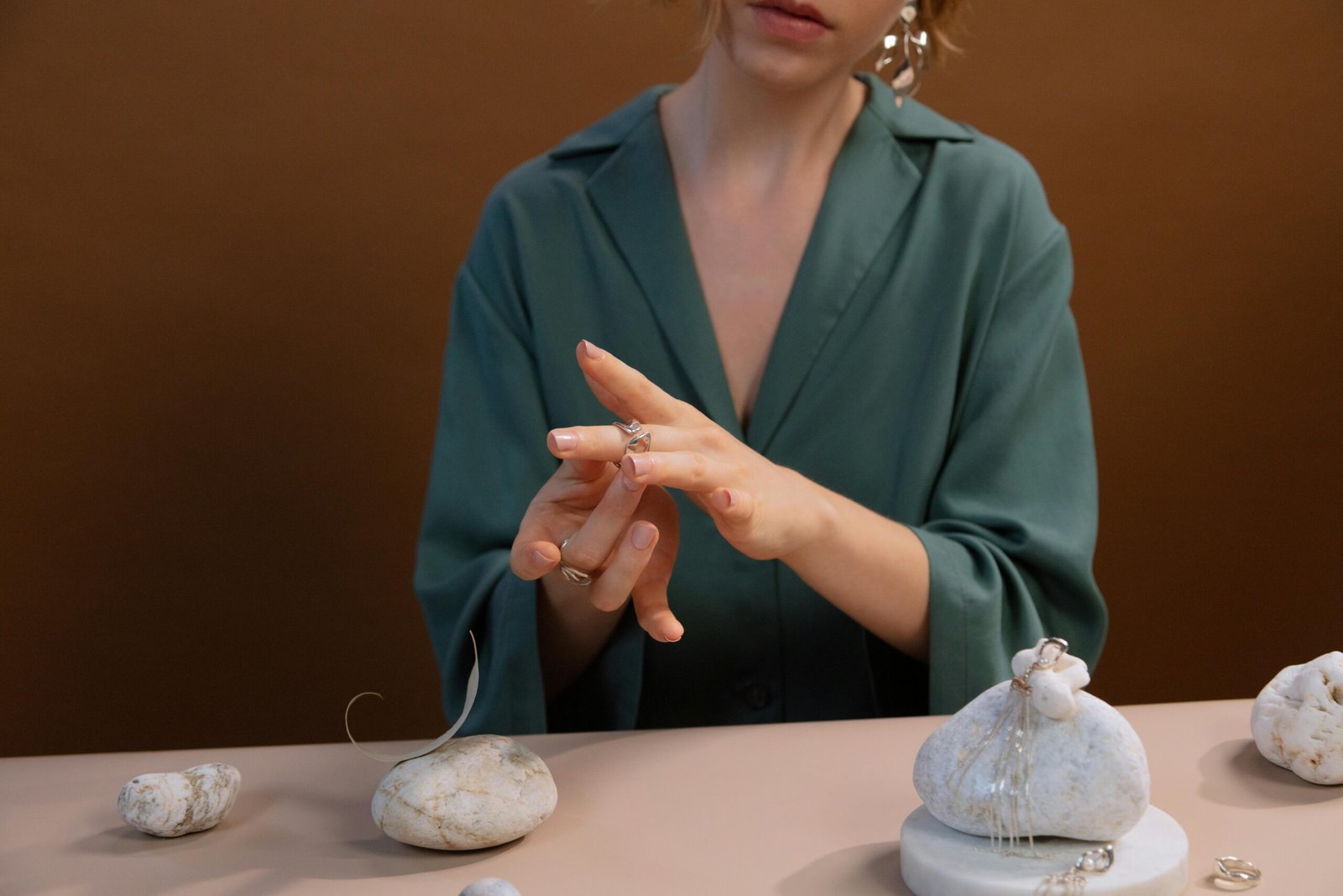 A woman trying on silver rings, showcasing elegant jewelry on a brown background.