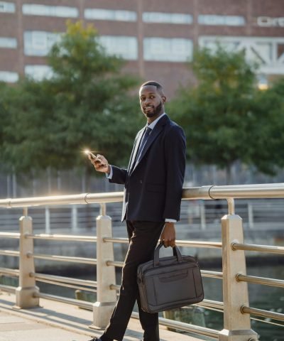 Professional in business attire using smartphone while walking on bridge in city setting.
